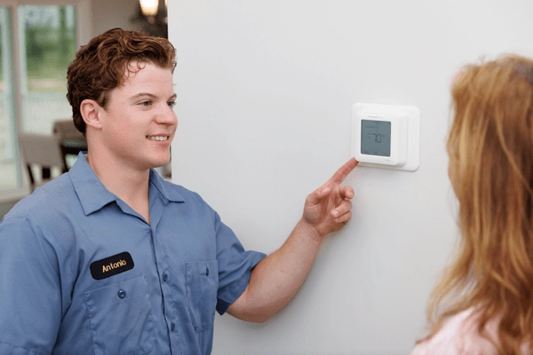 All American HVAC technician adjusting heat on thermostat
