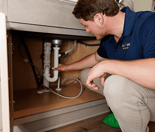 All American Heating, Air & Plumbing technician working on plumbing under a kitchen sink