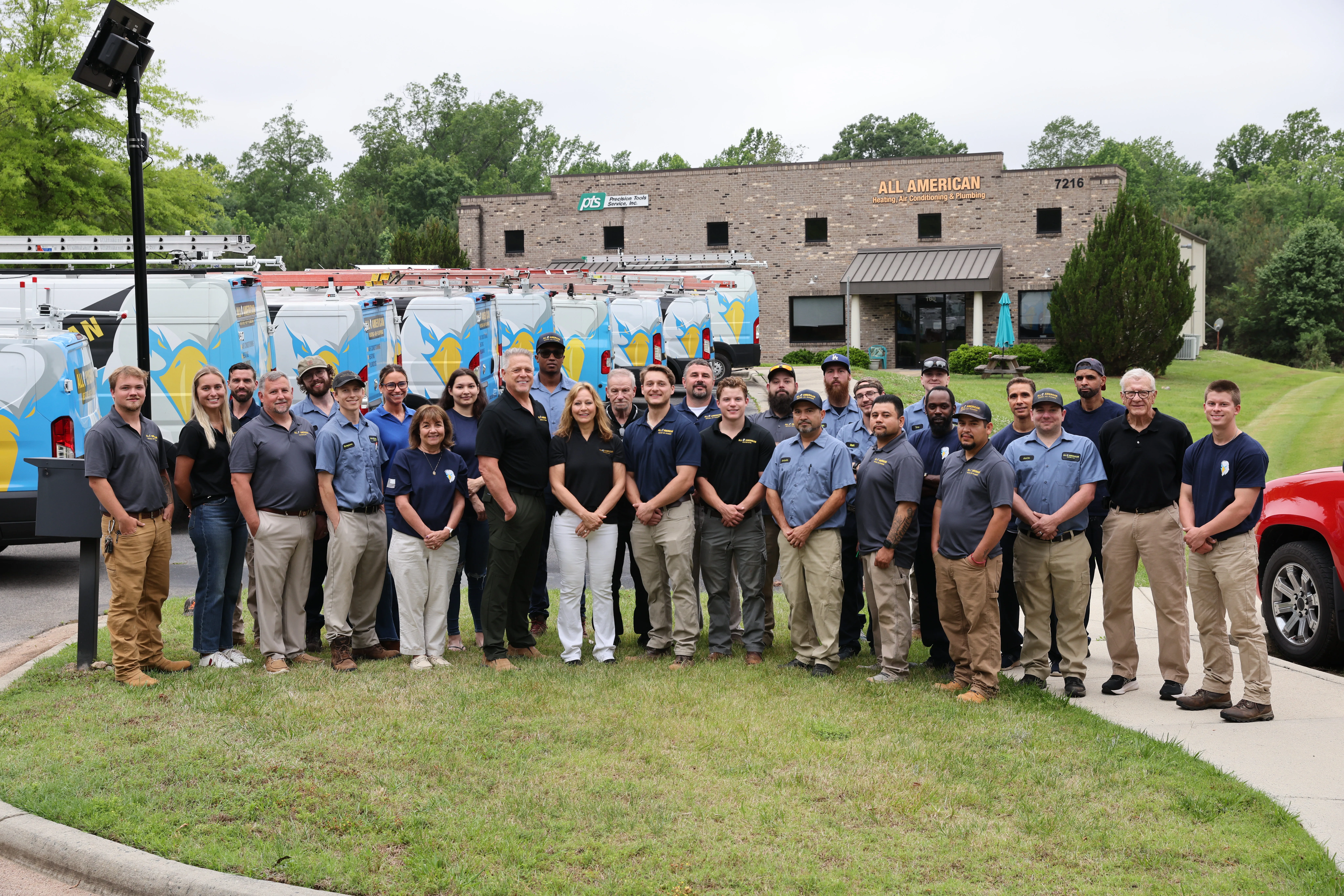 All American Heating, Air & Plumbing team photo in front of the office and branded service vans
