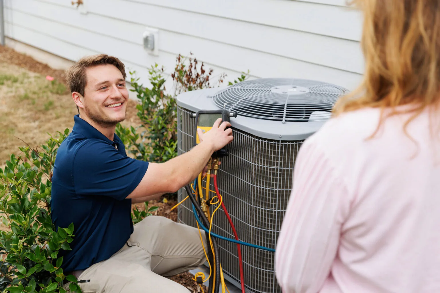 Technician servicing an AC condenser with homeowner present